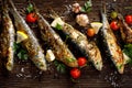 Fried fishes with addition of herbs, spices and lemon slices on a wooden background