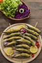 Fried horse mackerel `istavrit` fish skewered wooden sticks,on wooden plate with seasonal salad. Royalty Free Stock Photo