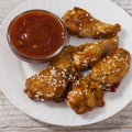 Fried juicy chicken wings marinated with honey, soy sauce, spices, sprinkled with sesame seeds on a white plate with sauce. Asian Royalty Free Stock Photo