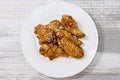 Fried juicy chicken wings marinated with honey, soy sauce, spices, sprinkled with sesame seeds on a white plate on a light Royalty Free Stock Photo