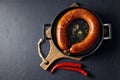 fried meat sausage in a cast iron pan and hot chili pepper on a cutting wooden board on a dark stone table Royalty Free Stock Photo