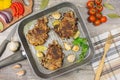 Fried meat slices in the pan, tomatoes greens onions garlic pepper, tasty food. Knife fork, on wooden table, background. Royalty Free Stock Photo