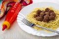 Fried meatballs with spaghetti, fork in dish, bottle with ketchup, napkin on wooden table