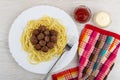 Fried meatballs with spaghetti, fork in dish, bowls with ketchup and mayonnaise, napkin on wooden table. Top view