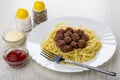 Fried meatballs with spaghetti, fork in dish, salt, pepper, bowls with ketchup and mayonnaise on wooden table