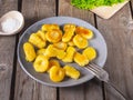 Fried potato gnocchi on a gray ceramic plate, leaves of fresh leaf lettuce lie on an unpainted kitchen board on an old plank Royalty Free Stock Photo