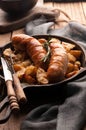 Fried potatoes and grilled sausages in pan with fork, knife, grey napkin and chopping board Royalty Free Stock Photo