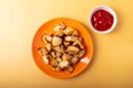 Fried potatoes on orange plate and a little ketchup bowl