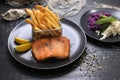 Fried rainbow trout fillet served with potato fries in a metal serving basket and salad, on black plates. Fish and chips