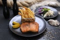 Fried rainbow trout fillet served with potato fries in a metal serving basket and salad, on black plates. Fish and chips