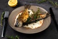 Fried rainbow trout fish with lemon sauce and thyme on black marble table as background close-up Royalty Free Stock Photo