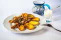 Fried sardines with baked potato on white plate with fork, garlic yogurt in glass, blue cup with drink