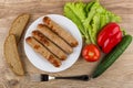 Fried sausage in plate, pepper, tomato, lettuce, bread and fork Royalty Free Stock Photo