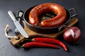 Fried sausage rolled into a ring on a cast iron pan with cutlery, a wooden cutting board, hot peppers and red onions Royalty Free Stock Photo