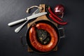 Fried sausage rolled into a ring on a cast iron pan with cutlery, a wooden cutting board, hot peppers and red onions Royalty Free Stock Photo