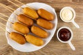 Fried sausages on skewers in white dish, sauce boats with mayonnaise and ketchup on table. Top view