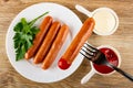 Fried sausages and parsley in plate, sausage with ketchup on fork, sauce boats with mayonnaise and ketchup on table. Top view