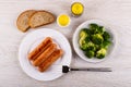 Fried sausages in plate, fork, broccoli in plate, bread, salt, pepper on table. Top view