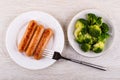 Fried sausages in plate, fork, broccoli in plate on table. Top view