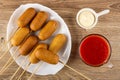 Fried sausages on skewers in dish, sauce boat with mayonnaise, cup with tomato juice on table. Top view