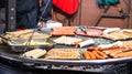 Fried sausages. Street eatery. Many grilled sausages on a large round barbecue grill at a street food festival. Barbecue Royalty Free Stock Photo