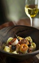 Fried sea scallops with seafood ravioli in a wooden dish with a white wine glass in the backgroun