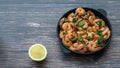 Fried shrimp in a creamy sauce top view in a cast iron pan on the table, next is half a lemon