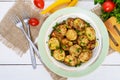 Fried slices of young zucchini with hot pepper, greens on a plate on a white wooden background.