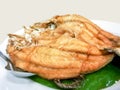 Fried snapper fish topped with fish sauce on banana leaf and white ceramic plate with stainless steel spoon.