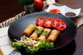 Fried spring rolls with vegetables and tomatoes placed in a black plate on a black wooden table and dipping sauce Royalty Free Stock Photo