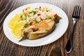 Fried steak from salmon with vegetable mix, slices of lemon in plate, fork on wooden table Royalty Free Stock Photo