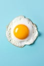 Fried sunny-side-up egg with bright yellow glossy yoke on light blue background. Culinary food concept