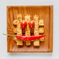 Fried tempeh decorated with chilly and tomato smile on a wooden tray. Top view. Close-up. Square image.