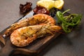 Fried tiger shrimps or langostinos with lemon, arugula, sun dried tomatos on a dark wooden cutting board. Placed on a background o Royalty Free Stock Photo