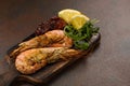 Fried tiger shrimps or langostinos with lemon, arugula, sun dried tomatos on a dark wooden cutting board. Placed on a background o Royalty Free Stock Photo