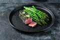 Fried tuna steak in black sesame with asparagus on black plate