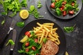 Fried Tuna Steaks on Black Plate with Fresh Green, Tomato Salad, lemon and french fries. healthy sea food Royalty Free Stock Photo