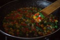 Fried vegetable mix on black skillet. Stewed sliced vegetables on a pan. Frozen vegan breakfast preparation. Using paddle
