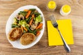 Fried vegetable mix and cutlets in white dish, fork on yellow napkin, salt and pepper on wooden table. Top view Royalty Free Stock Photo