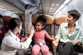 Friendly air hostess take care and help kid passenger on airplane, cheerful flight attendant and curly hair African girl giving Royalty Free Stock Photo