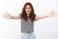 Friendly amazed cute redhead caucasian girl in striped t-shirt extend arms sideways, move towards camera to give hug