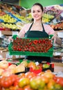 Friendly attractive saleswoman with crate with tomatoes in supermarket