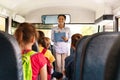 Friendly black female teacher checking off children names sitting inside school bus