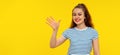 Friendly brunette girl smiling, saying hi and waving hand to greet person, welcome someone, standing in white-blue striped t shirt Royalty Free Stock Photo