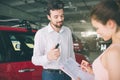 Friendly car salesman talking to a young woman and showing a new car inside showroom Signing of contract