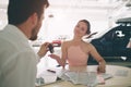 Friendly car salesman talking to a young woman and showing a new car inside showroom Signing of contract.