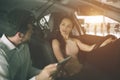 Friendly car salesman talking to a young woman and showing a new car inside showroom Signing of contract.