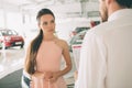 Friendly car salesman talking to a young woman and showing a new car inside showroom Signing of contract.