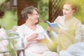 Friendly caregiver reading a book and senior woman drinking tea Royalty Free Stock Photo