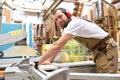 friendly carpenter with ear protectors and working clothes working on a saw in the workshop